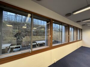 Interior office space with large windows overlooking the outdoor seating area and vegetation at De Ruijterkade.